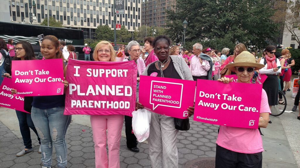 A crowd holds hot pink signs in support of Planned Parenthood and reproductive healtchare.