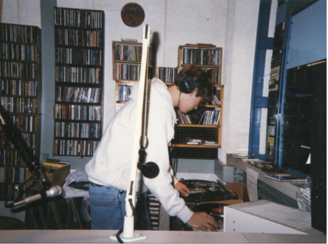 A student wearing headphones adjusts the needle of a record player inside the WPTS student radio station.