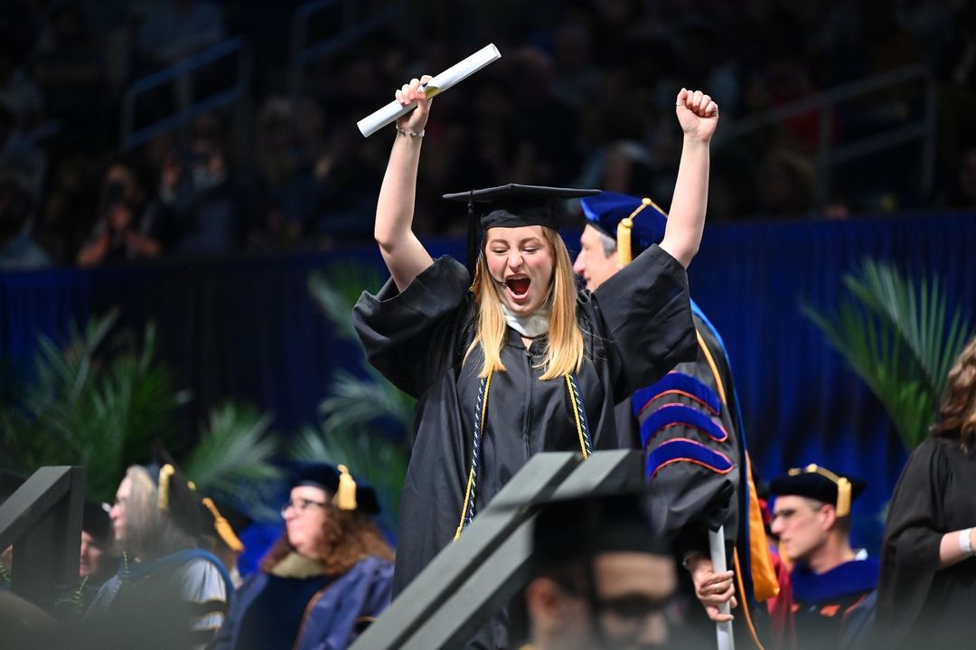 A 2024 Pitt grad holding a diploma cheers.