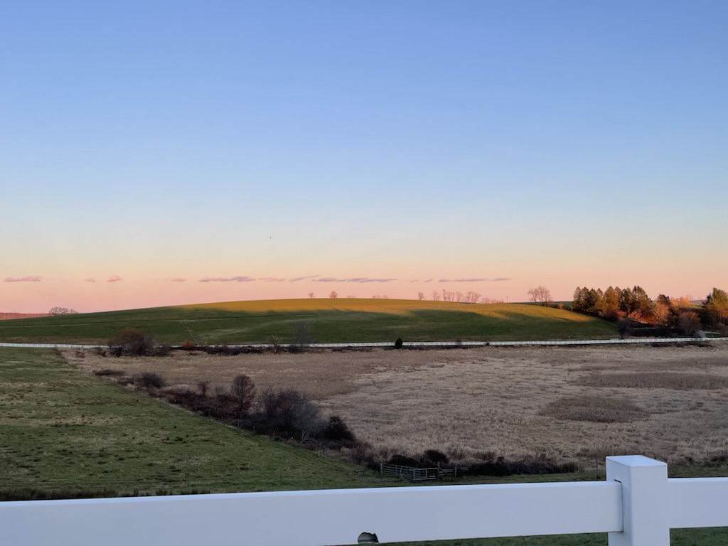 A view of Horsebarn Hill from Storrs Road in Connecticut, featuring a blue and pink sunset over a field with white fences