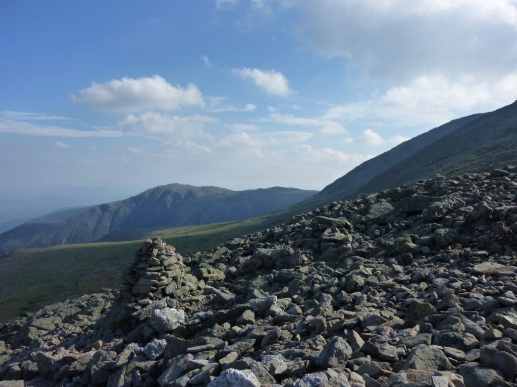 View of a rock cairn on Mount Washington in the White Mountains, with sky and mountains in the background